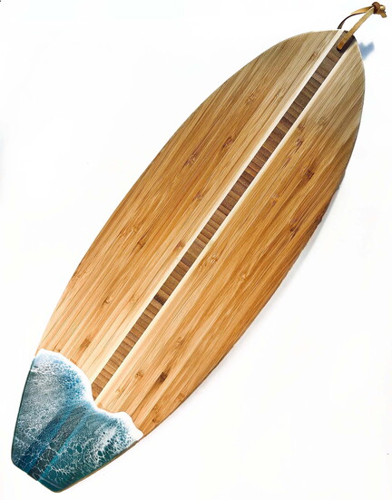 Surfboard-shaped bamboo cutting board accented with an ocean resin design.