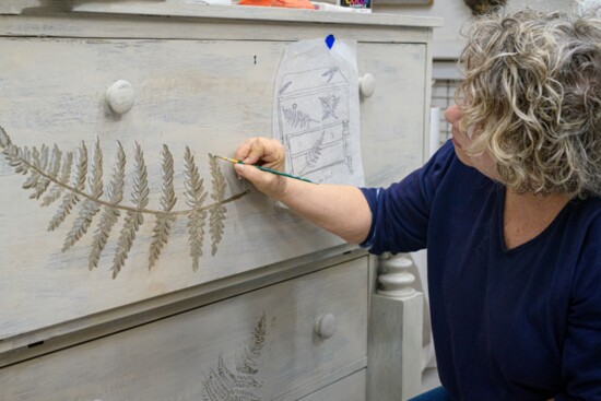 Merri paints a fern design onto a reworked dresser
