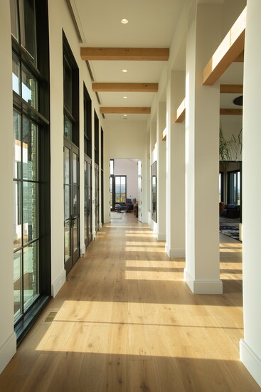 Expansive hallways use floor-to-ceiling windows and exposed beams to create light-filled transitions between the interior and outdoors.