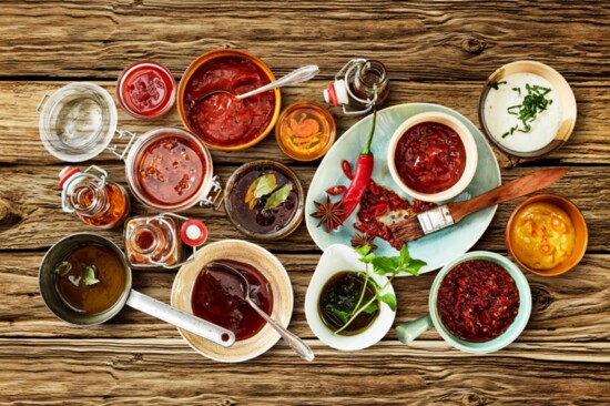 Various white bowls with delicious red sauce and chutney near assorted herbs and peppers