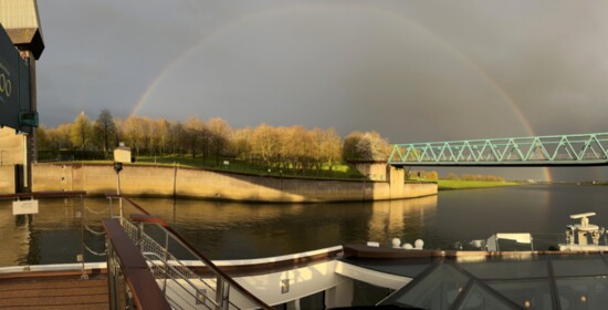 An early-morning rainbow arches over the Netherland canal and countryside.