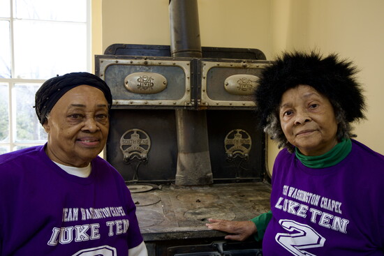 Pearl Douglass Spencer and Dr. Cora Douglass Thompson stand before the antique stove where their grandmother once prepared meals at the church. 