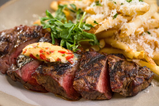 Steak frites pairs a perfectly cooked New York strip with truffle-herb butter and parmesan fries.