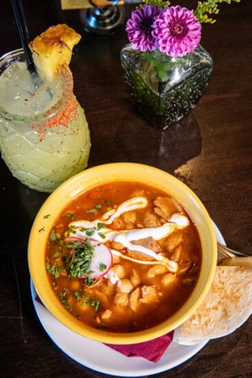 The Red Chicken Pozole at Tiho's consists of red chile chicken broth and hominy, topped with shaved radish, minced red onion, Cotija cheese, and cilantro. 