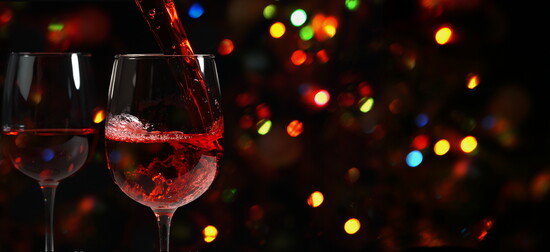 Red wine being poured with a backdrop of holiday lights.