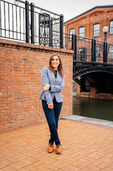 Kate stands along Carroll Creek Linear Park, framed by historic brick buildings and the city's charm. 