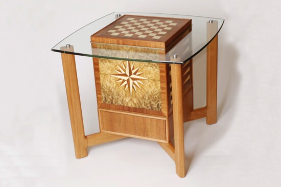 Game cube table serves as a game table for chess, checkers, backgammon, and Scrabble when the cube is turned to expose the desired game. Original design.